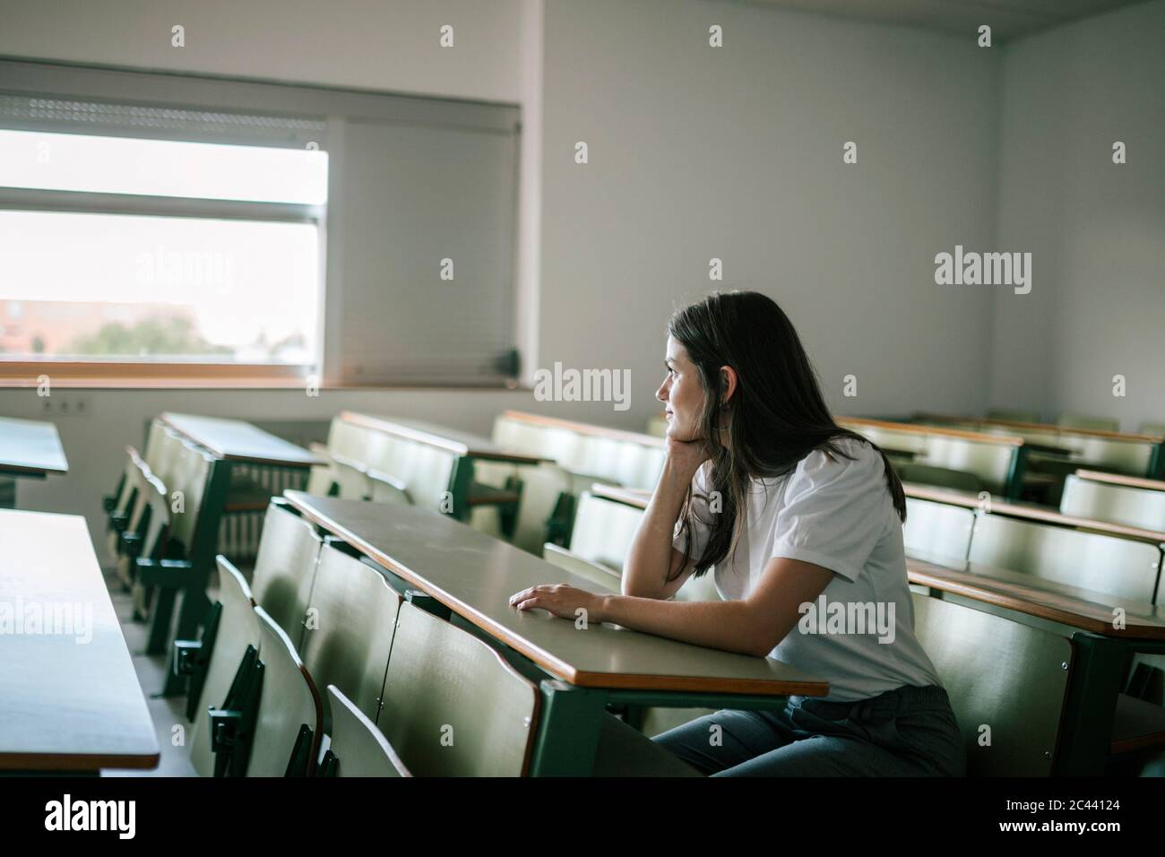 Donna giovane e premurosa che guarda lontano mentre si siede alla scrivania Foto Stock