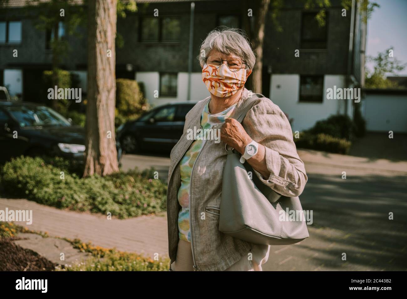 Donna anziana che indossa la maschera mentre si trova all'aperto durante la giornata di sole durante l'epidemia Foto Stock