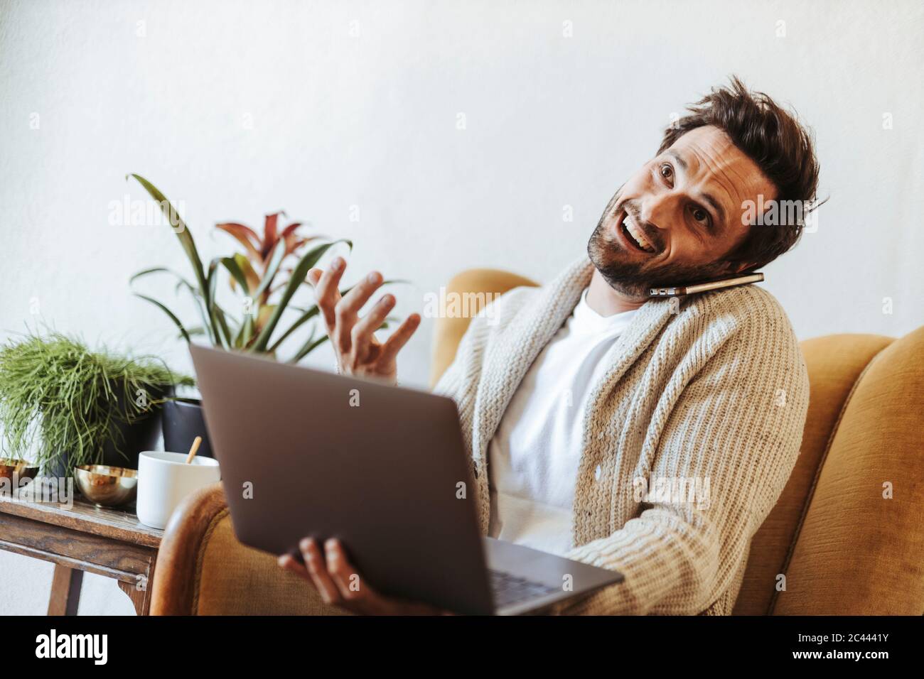 Ritratto dell'uomo sul telefono seduto sulla poltrona con il computer portatile che tira i volti divertenti Foto Stock