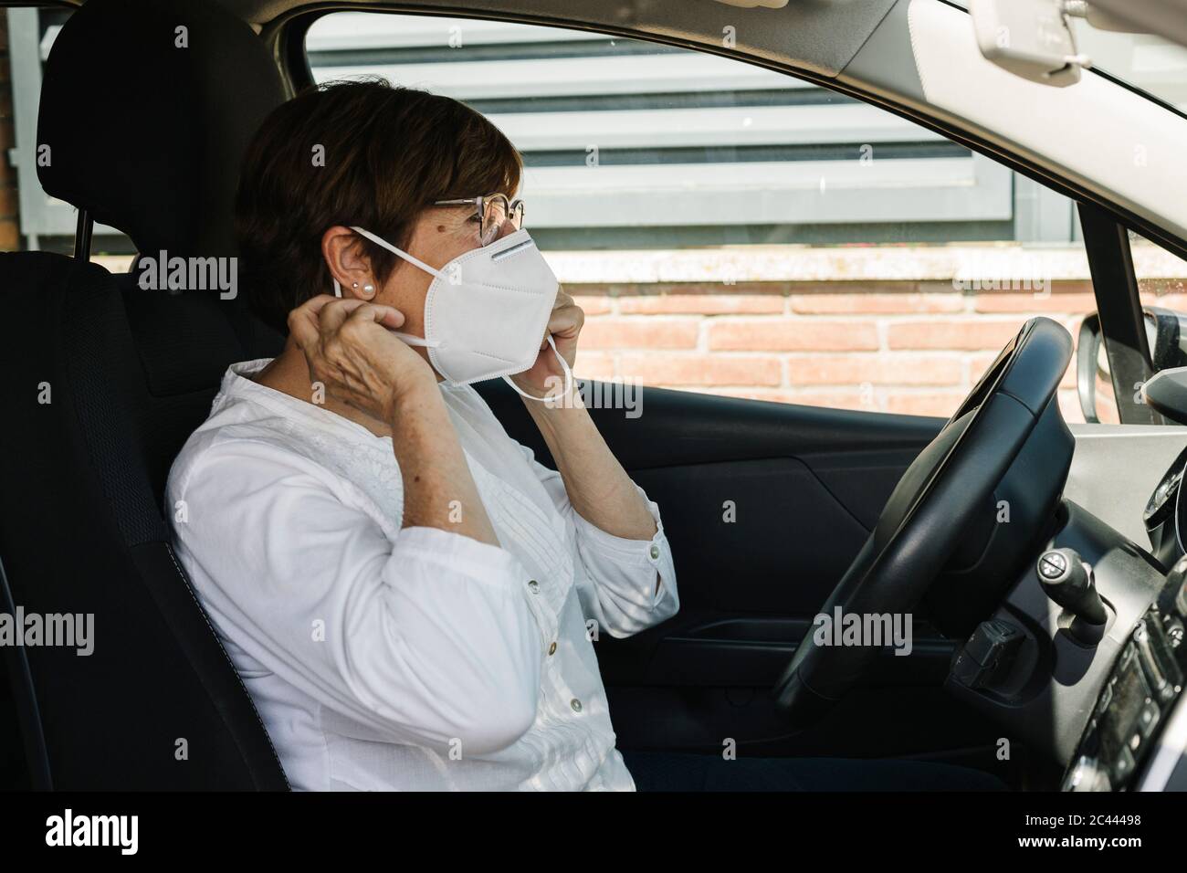 Donna che mette sulla maschera in auto Foto Stock
