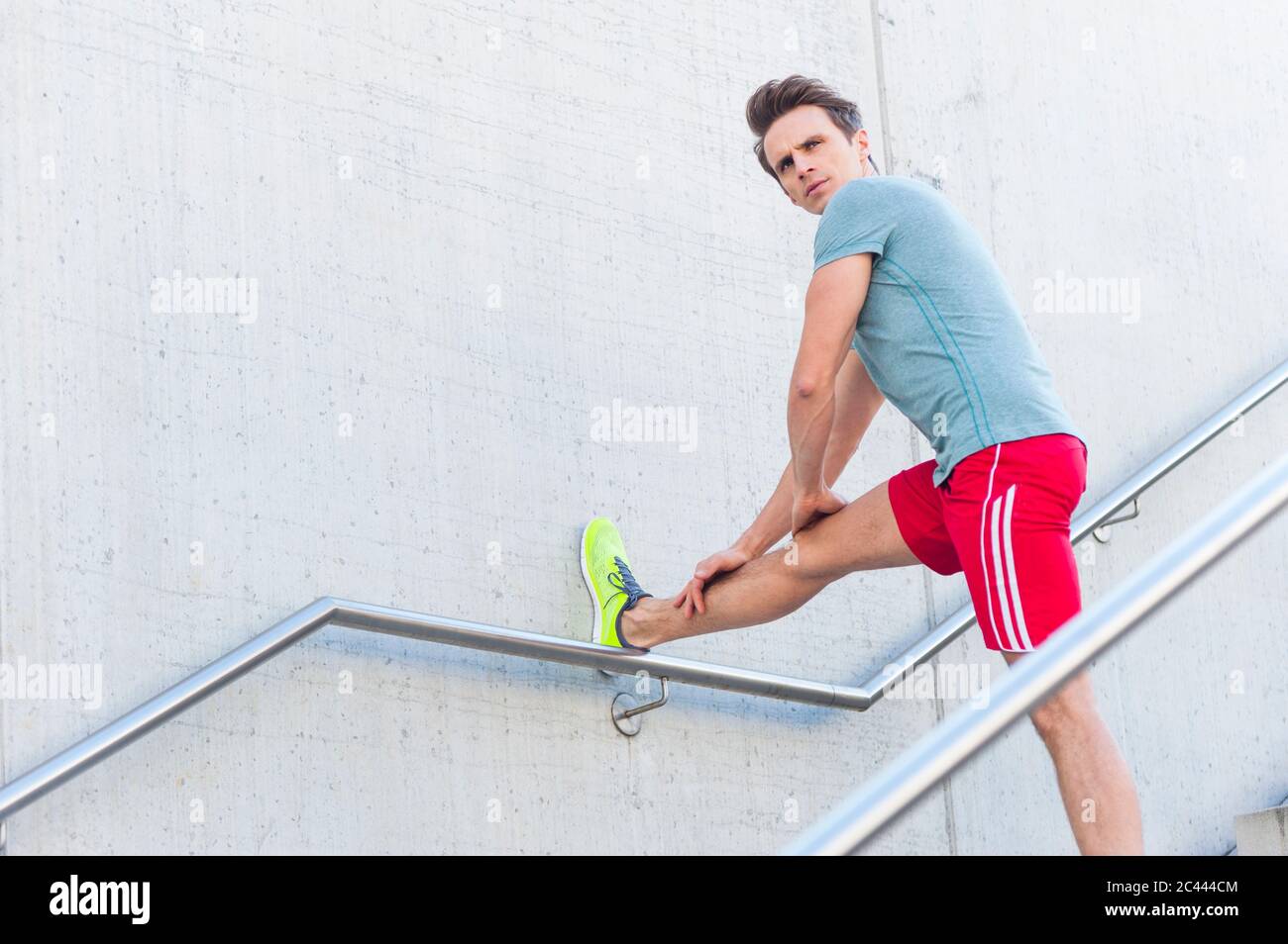 Bell'uomo medio adulto che allunga la gamba sulla parete mentre si alza sopra i gradini Foto Stock
