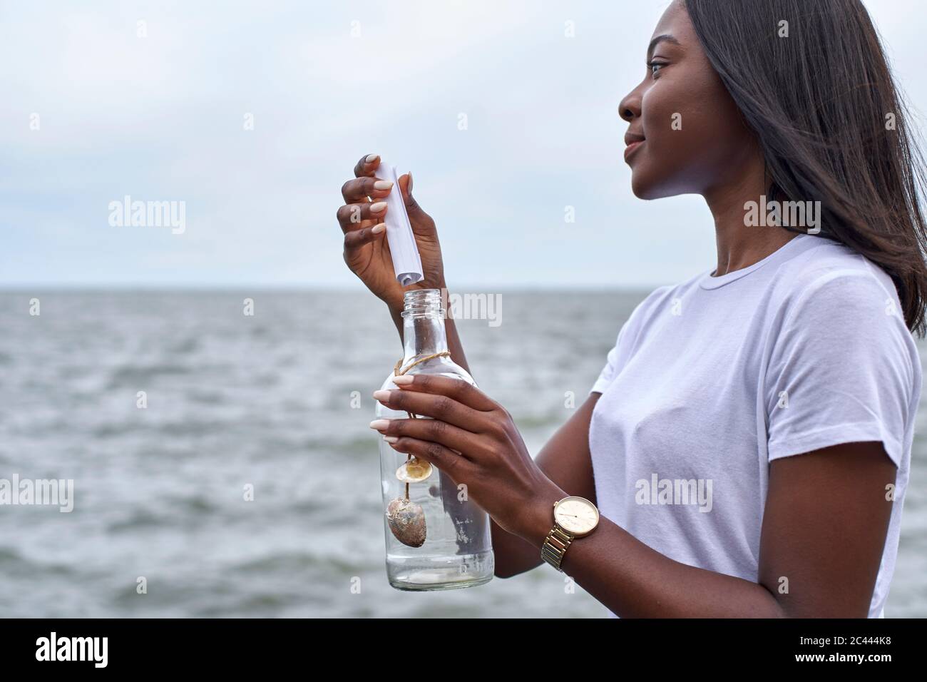 Profilo di giovane donna di fronte al mare inviando messaggio in bottiglia Foto Stock