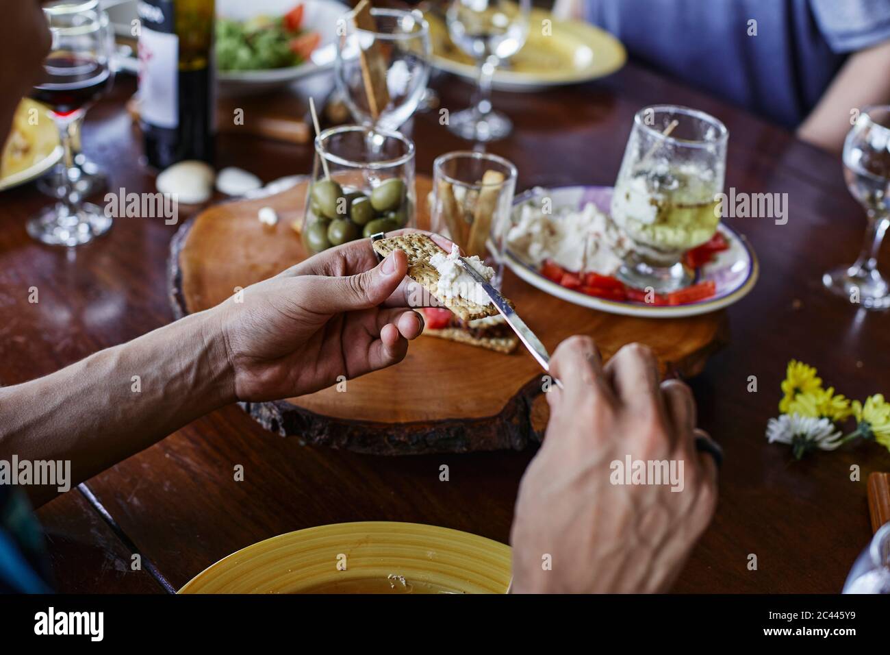 Mani tagliate di uomo che stese il formaggio sul cracker al tavolo da pranzo Foto Stock