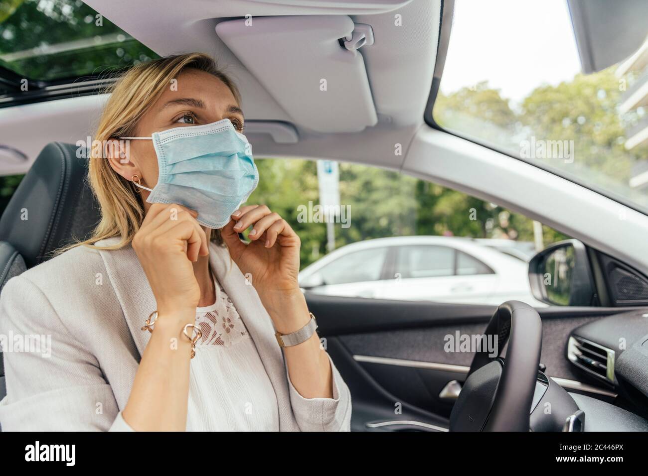 Ritratto di donna in auto che mette su maschera protettiva Foto Stock