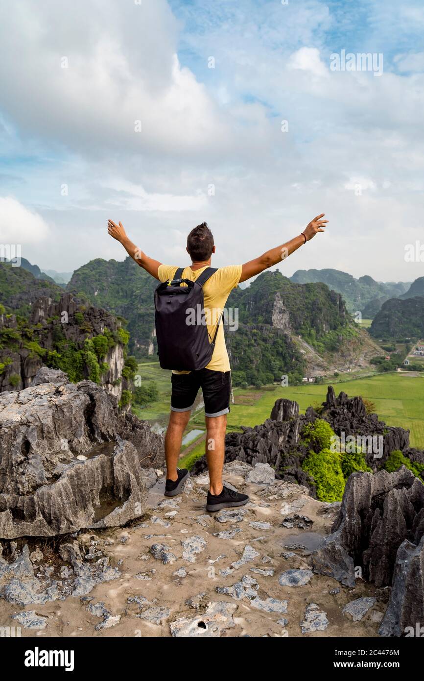 Vietnam, Provincia di Ninh Binh, Ninh Binh, escursionista maschile in piedi con braccia rialzate al bordo della formazione carsica del Delta del fiume Hong Foto Stock