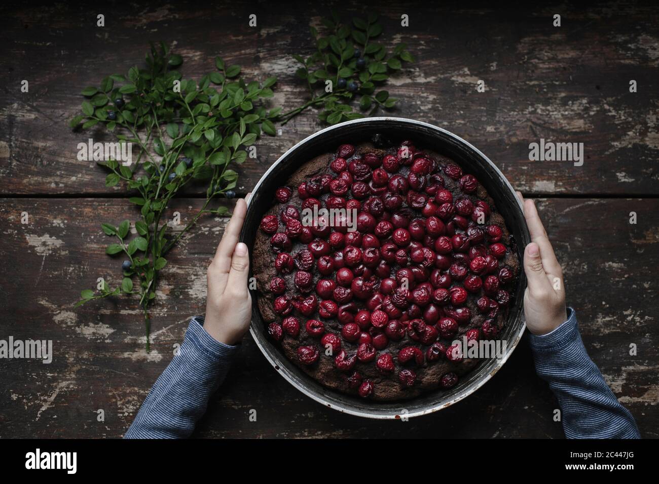 Mani tagliate di boy holding cherry brownie torta sul tavolo di legno Foto Stock