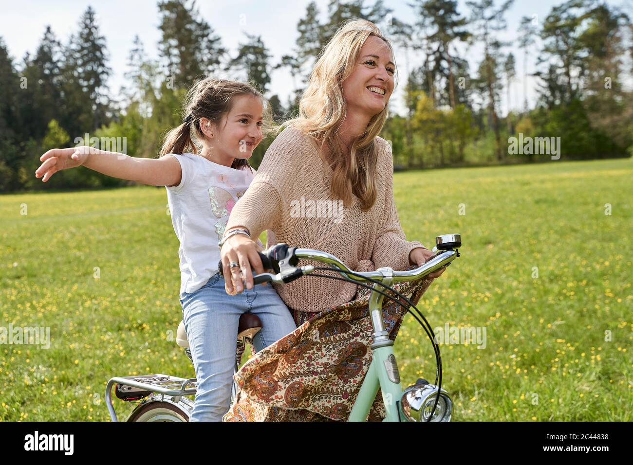 Ragazza con le braccia allungate godendo di giro in bicicletta con la madre sulle piante Foto Stock