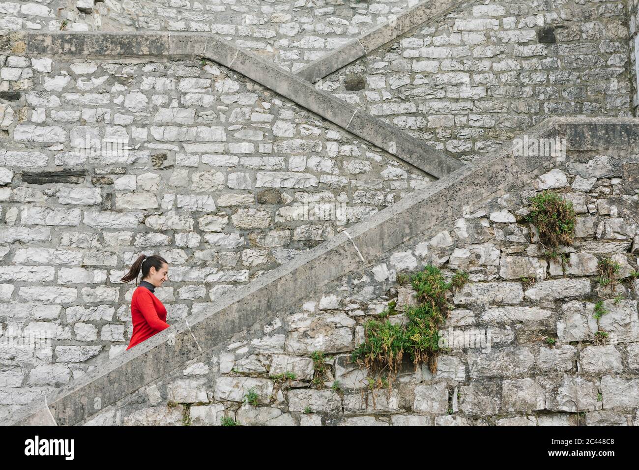 Vista laterale di una donna sorridente che si muove su una scala, Itzurun, Zumaia, Paesi Baschi spagnoli, Spagna Foto Stock