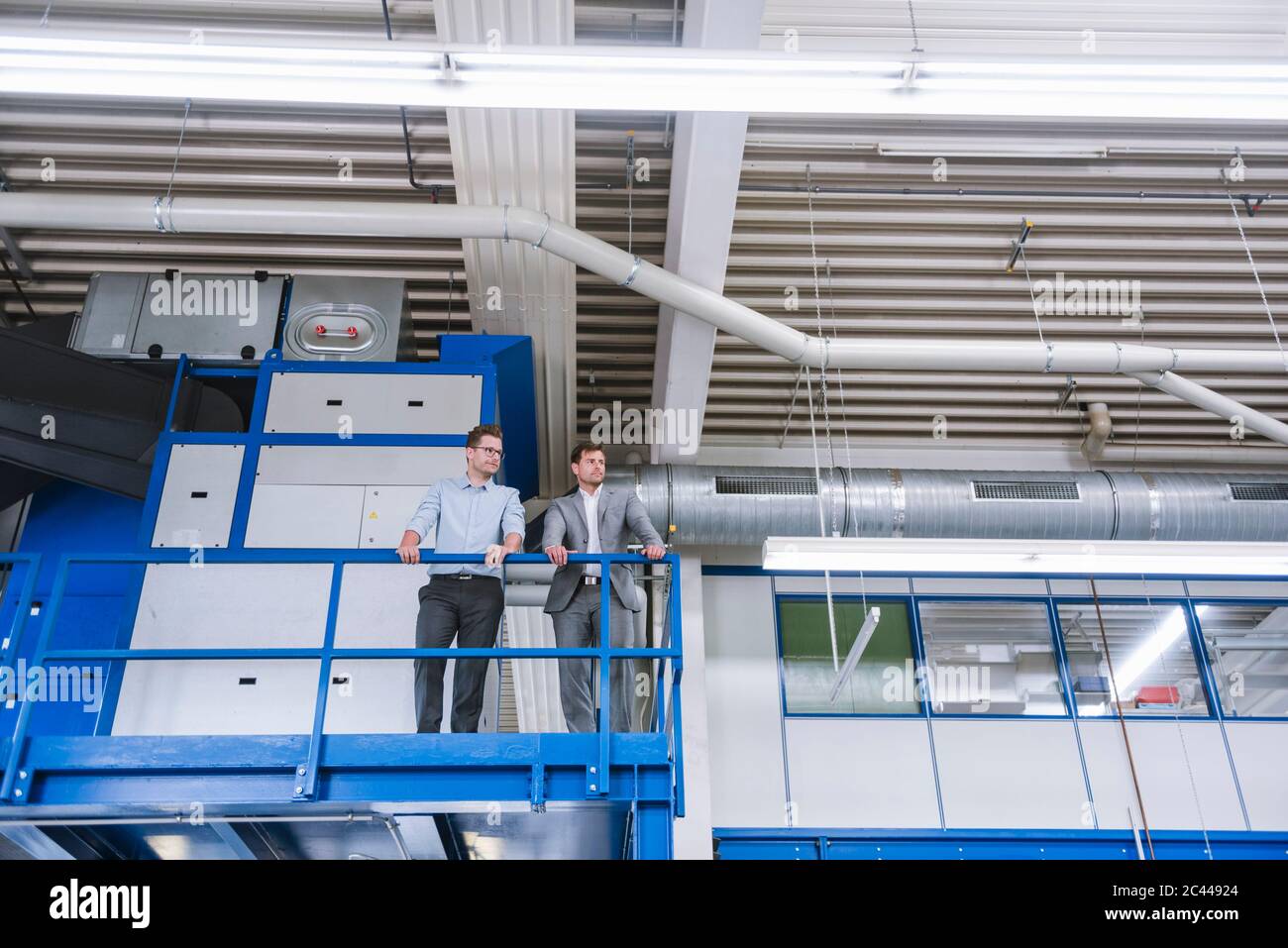 Due uomini d'affari in piedi al piano superiore in una fabbrica Foto Stock