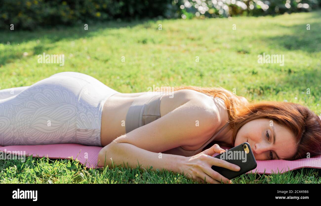 Giovane donna che si stette su un tappetino in erba controllando il telefono cellulare Foto Stock