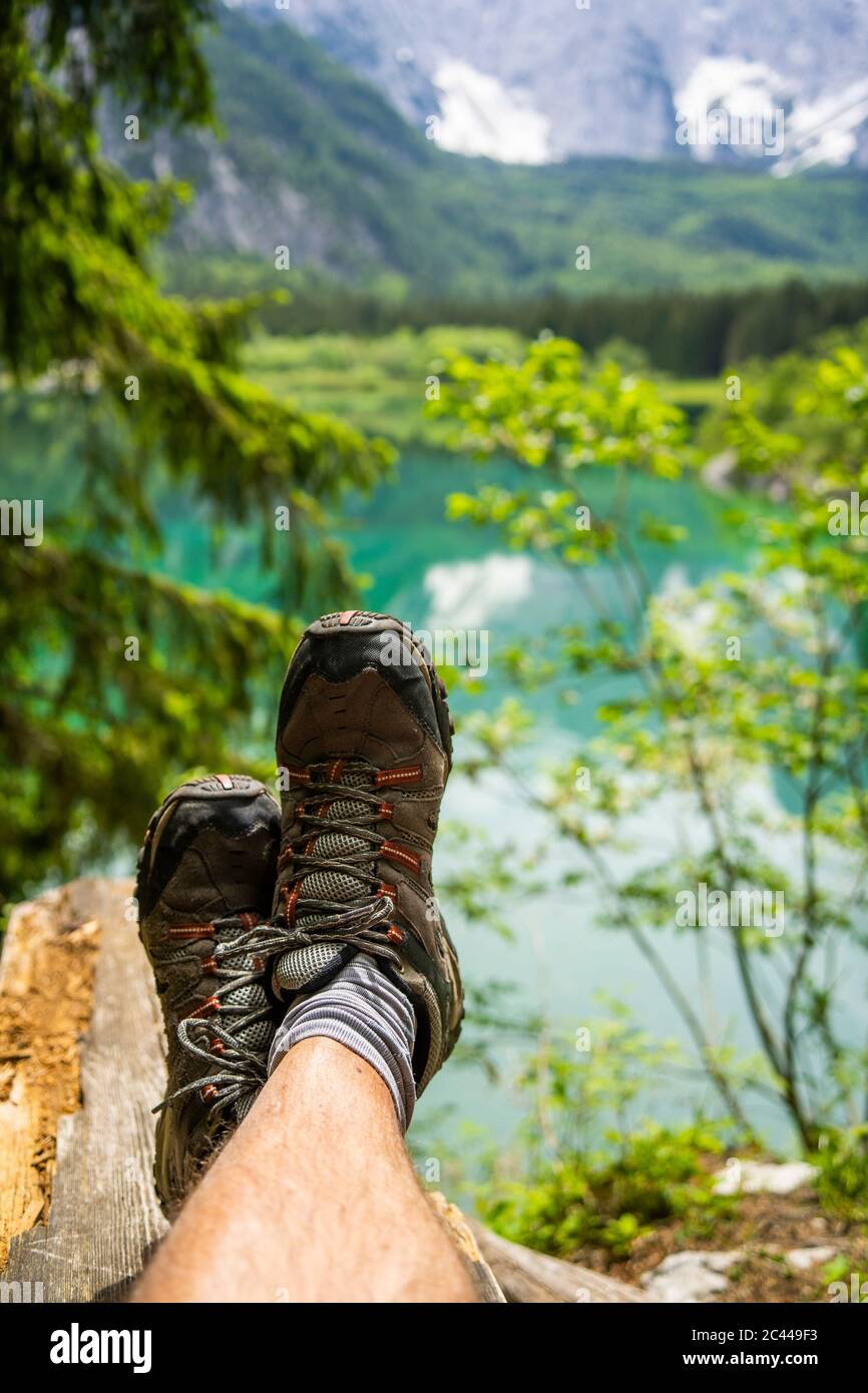 Italia, Provincia di Udine, Tarvisio, piedi di uomo che indossa scarpe da trekking rilassante sulla riva del lago Fusine Foto Stock