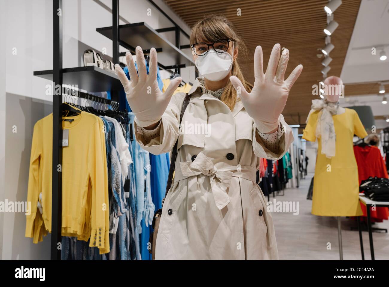 Donna con maschera facciale e guanti monouso che acquista in un negozio di moda Foto Stock