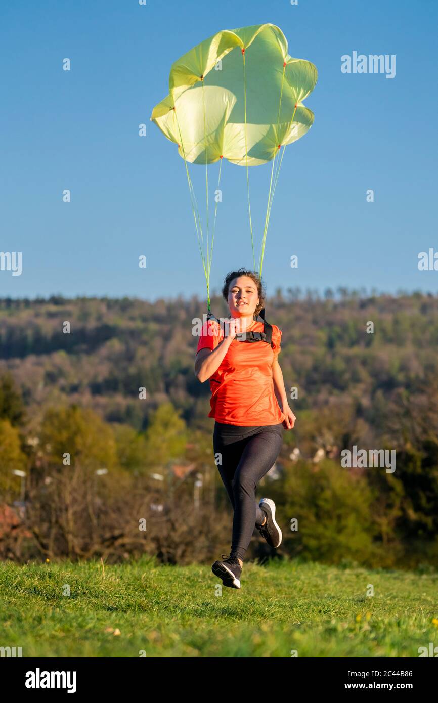 Tutta la lunghezza della giovane donna che si sprint con paracadute sull'erba contro il cielo limpido Foto Stock