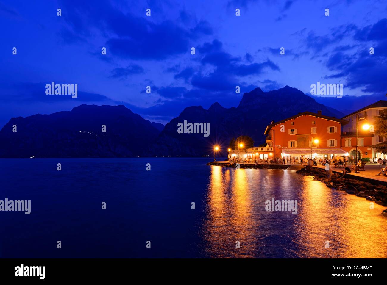 Italia, Trentino, Torbole, Lago di Garda, passeggiata e città illuminate al tramonto Foto Stock