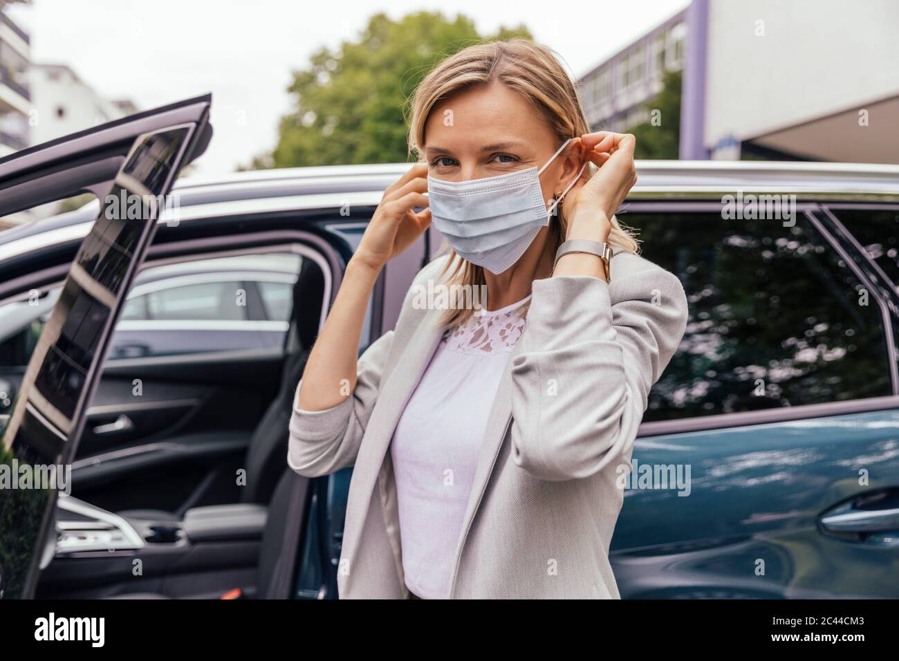 Ritratto di donna in piedi davanti alla sua auto mettendo su maschera protettiva Foto Stock
