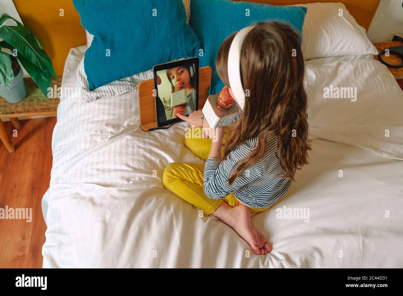 Ragazza che canta con il micro e usa il tablet per un video a letto Foto Stock