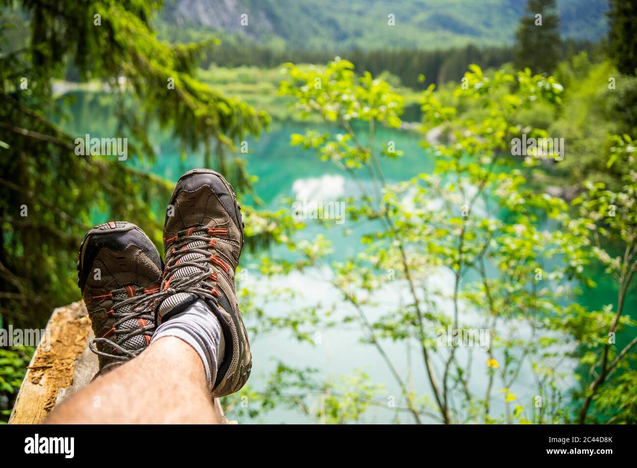 Italia, Provincia di Udine, Tarvisio, piedi di uomo che indossa scarpe da trekking rilassante sulla riva del lago Fusine Foto Stock