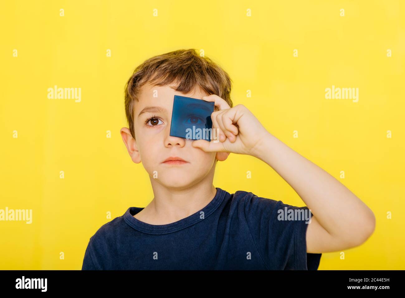 Primo piano di un ragazzo carino che tiene il vetro acrilico blu su sfondo giallo Foto Stock