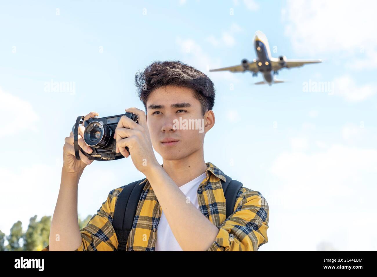 Ritratto di giovane turista con macchina fotografica con aereo sopra di lui Foto Stock