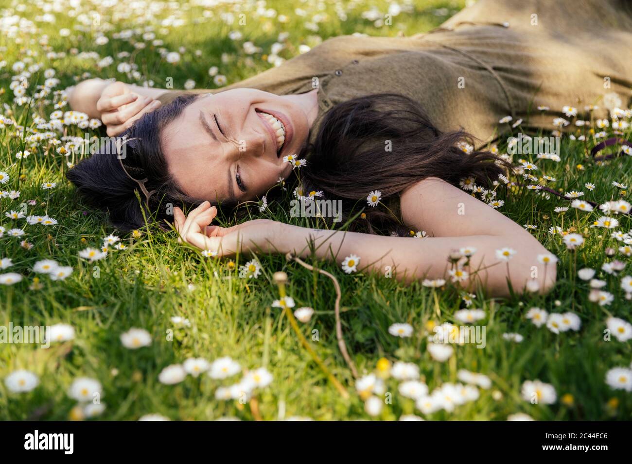 Donna felice godendo il suo tempo libero mentre si sdraiava su erba con margherite Foto Stock