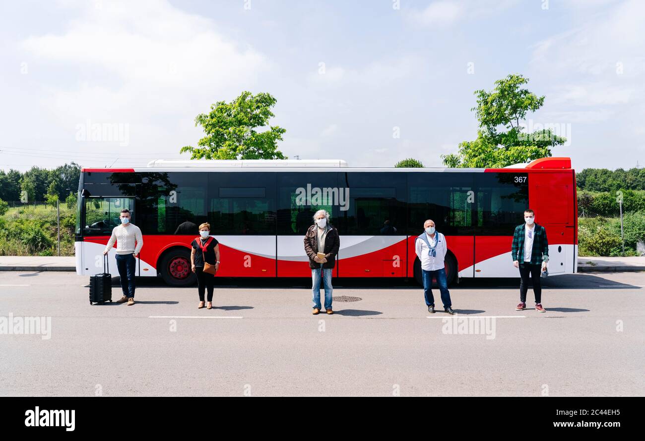 Cinque passeggeri che indossano maschere di protezione in piedi di fila davanti al bus pubblico, Spagna Foto Stock