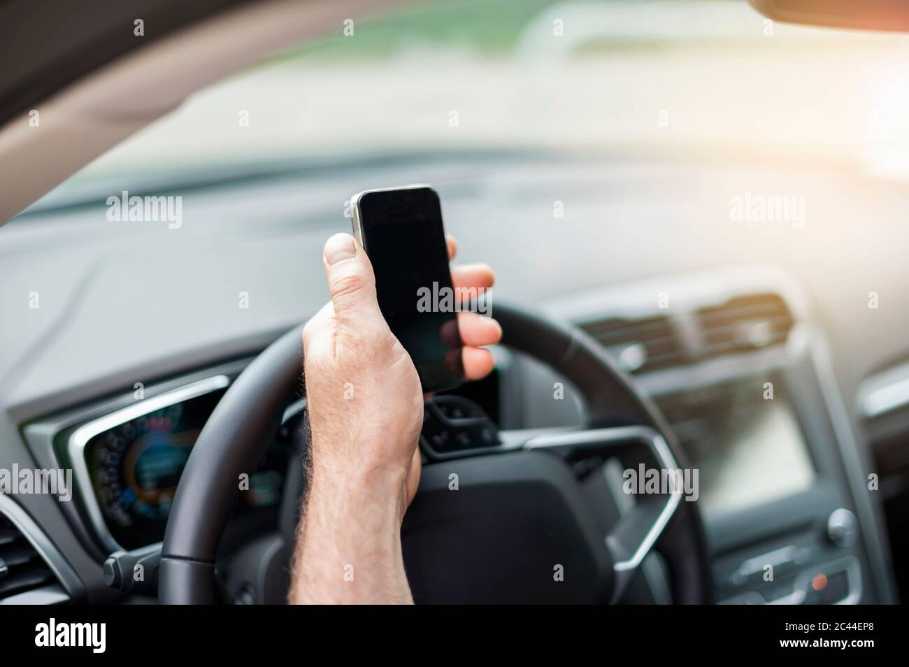 Mano tagliata di un uomo che tiene lo smartphone sul volante in auto Foto Stock
