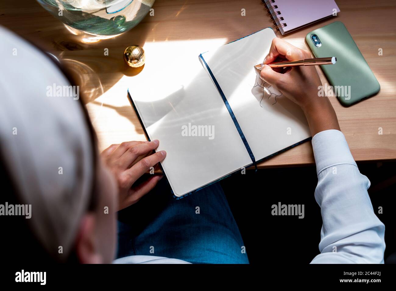 Donna mid adulta che si sta dipingendo in diario sulla scrivania a casa Foto Stock