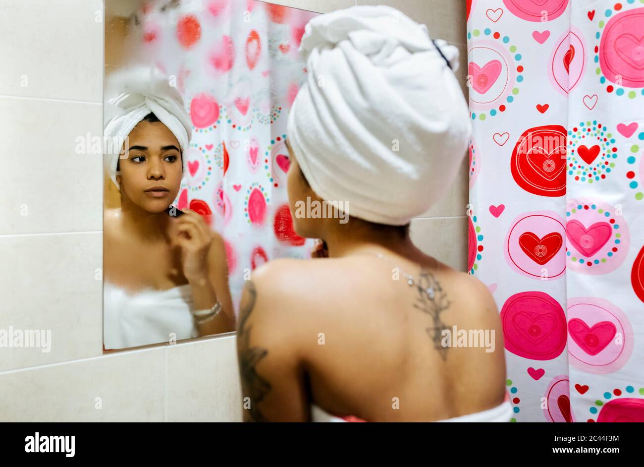 Giovane donna che guarda nello specchio del bagno che applica il trucco Foto Stock