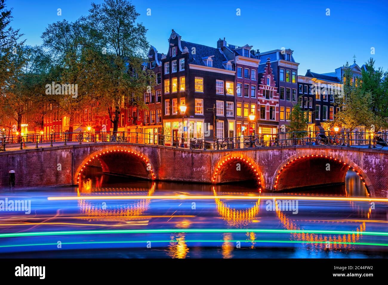 Olanda, Olanda del Nord, Amsterdam, sentieri luminosi di fronte al ponte illuminato vecchio della città al tramonto Foto Stock