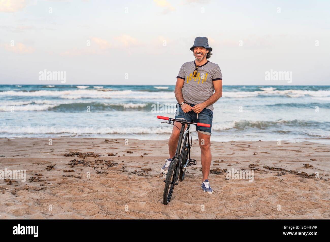 Uomo maturo seduto in bicicletta sulla spiaggia Foto Stock