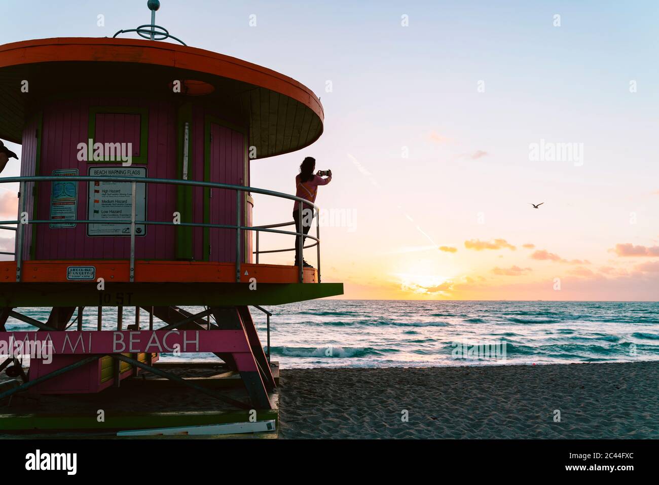 Donna che fotografa il mare dalla capanna bagnino all'alba, Miami Beach, Florida, USA Foto Stock