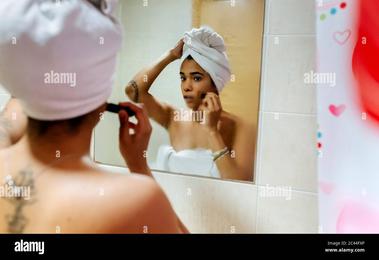 Giovane donna che guarda nello specchio del bagno che applica il trucco Foto Stock