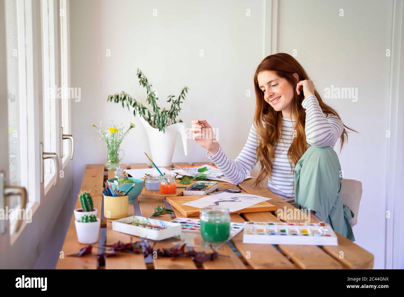 Felice giovane donna pittura con vernici acquerello sul tavolo a casa Foto Stock