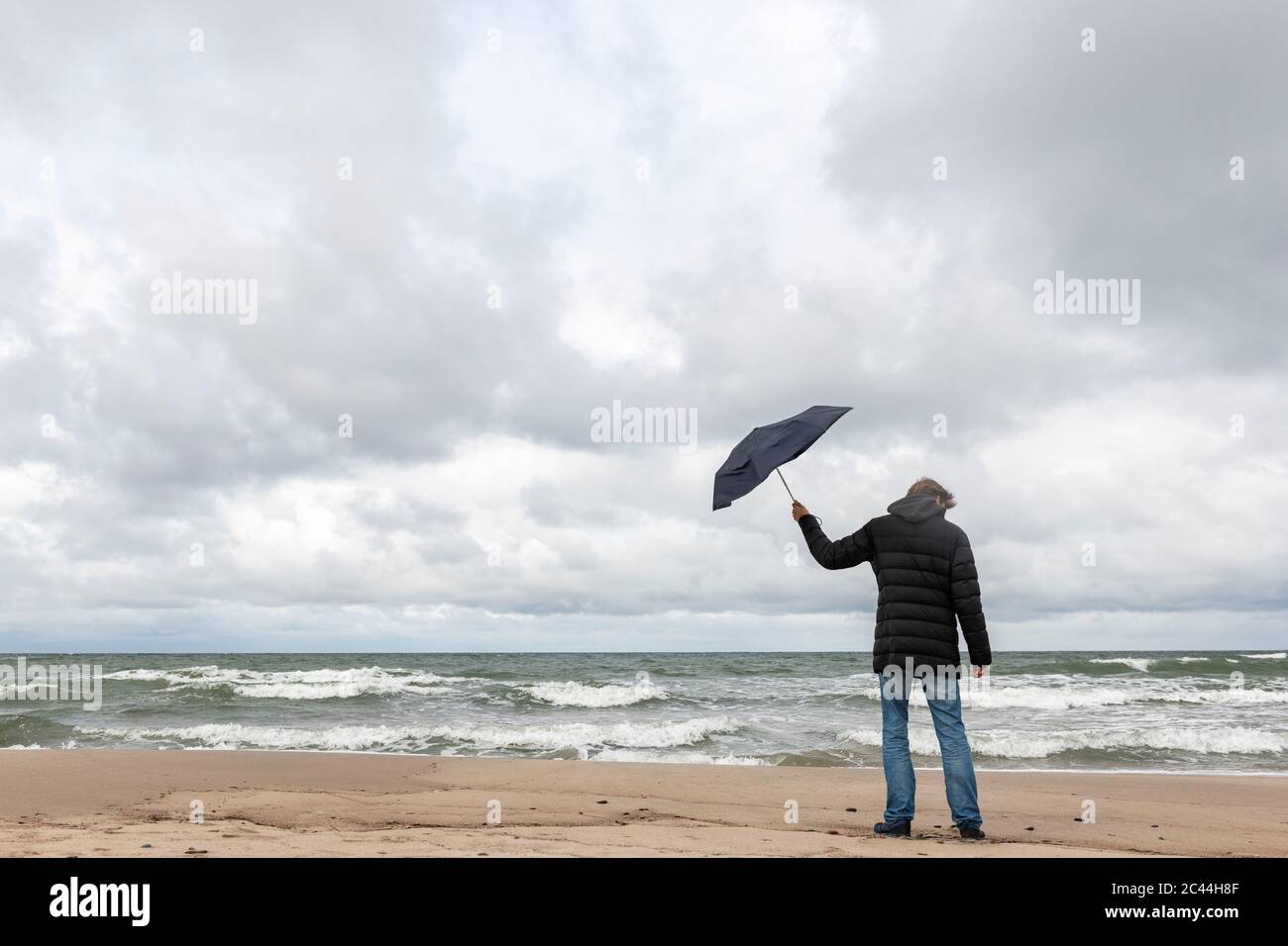 Russia, Kaliningrad Oblast, Zelenogradsk, uomo in piedi sulla spiaggia sabbiosa costiera con ombrello in mano Foto Stock