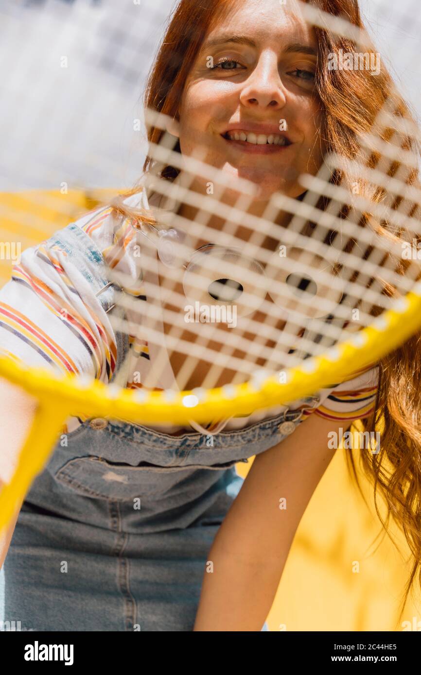 Felice giovane donna che guarda attraverso la racchetta di badminton durante la giornata di sole Foto Stock