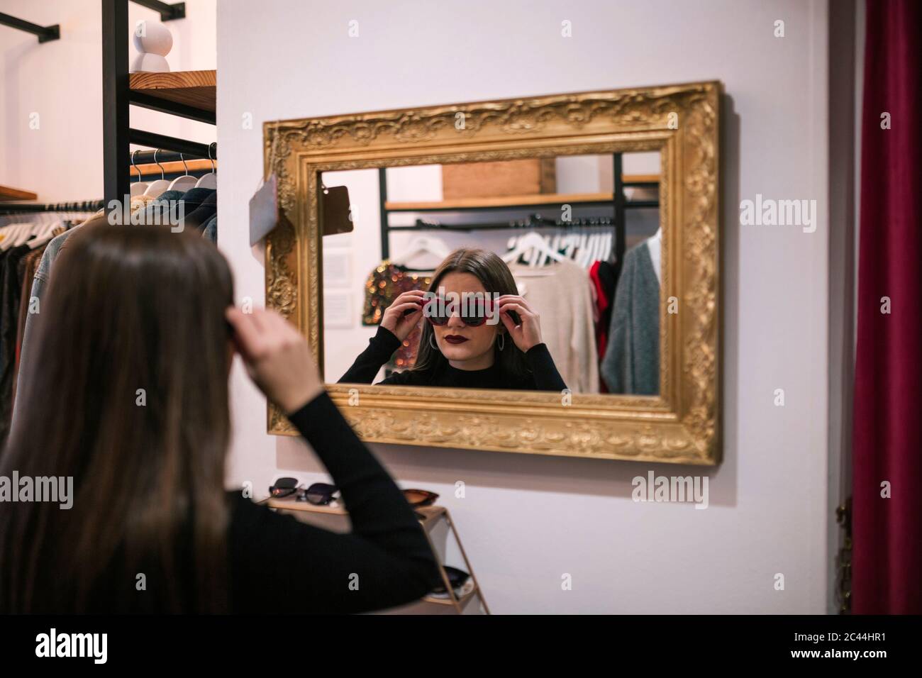 Immagine speculare di un giovane cliente che indossa occhiali da sole in un negozio di moda Foto Stock