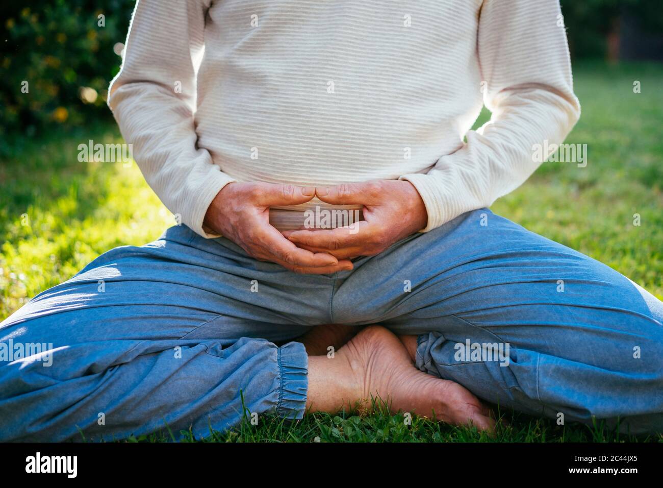 Sezione bassa dell'uomo anziano meditando in giardino Foto Stock