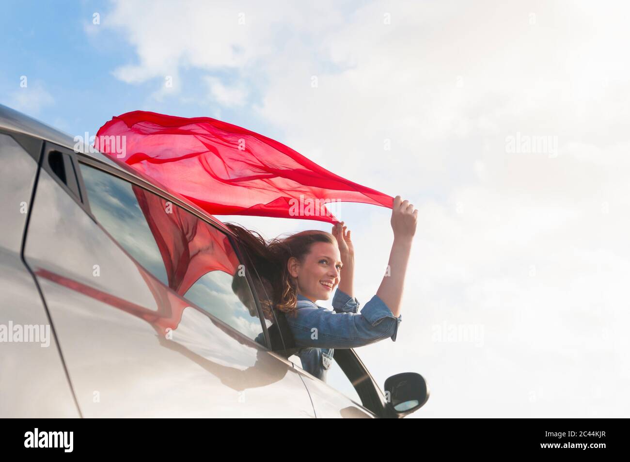Ritratto di donna sorridente che si appoggia fuori dal finestrino dell'auto tenendo un panno rosso, Sardegna, Spagna Foto Stock