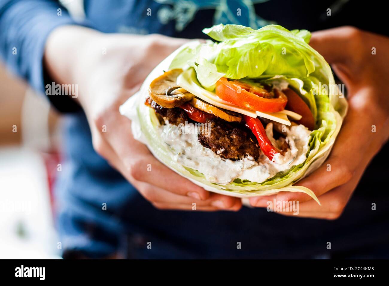 Le mani della persona che tiene il carburatore basso burger con bun insalata di verdure arrosto e salsa tzatziki Foto Stock