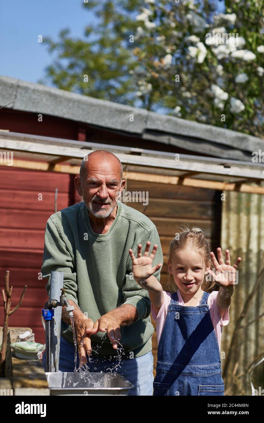Ritratto di ragazza con nonno in giardino di assegnazione mostrando le sue mani pulite dopo il lavaggio Foto Stock