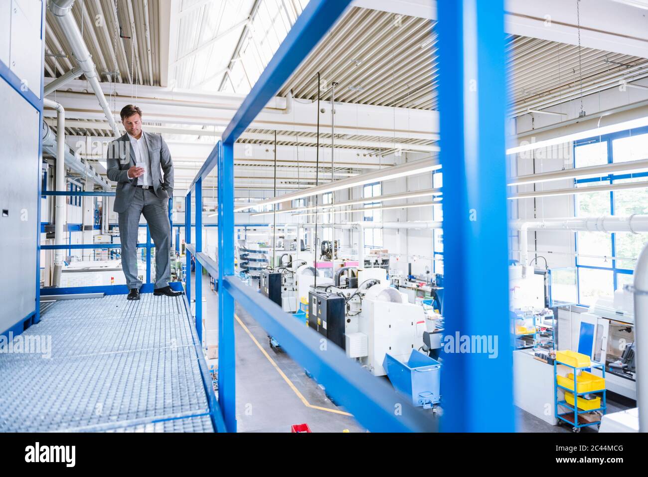 Uomo d'affari che utilizza uno smartphone al piano superiore in una fabbrica Foto Stock