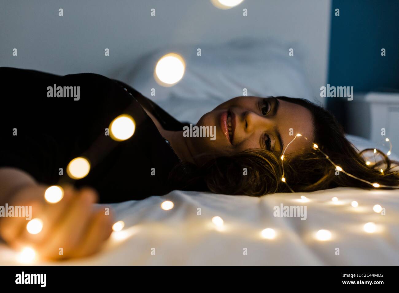 Donna giovane felice con sindrome di Down sdraiata sul letto illuminato a casa Foto Stock