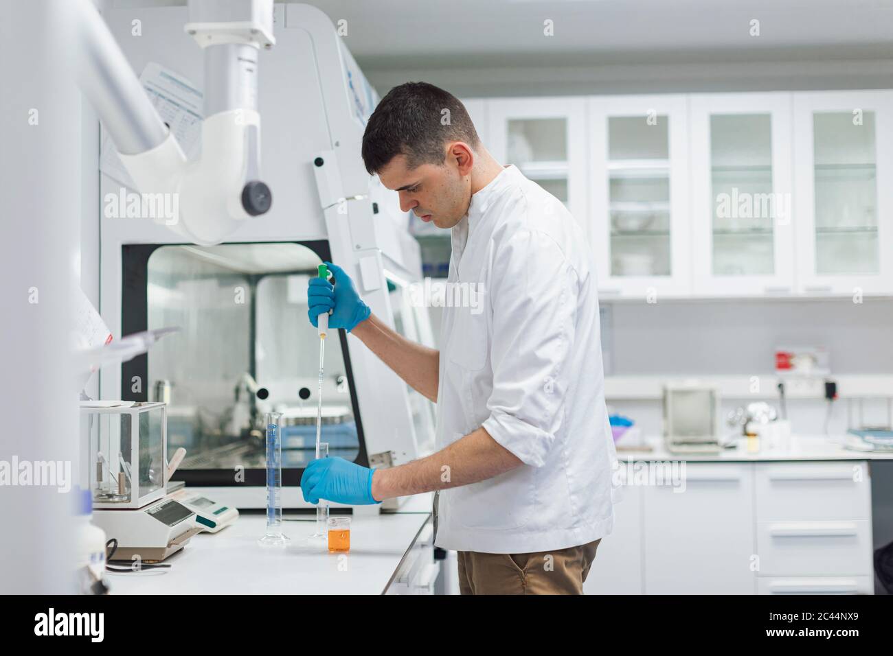 Giovane scienziato maschile che prende sostanze chimiche con la pipetta mentre si svolge la ricerca in laboratorio Foto Stock