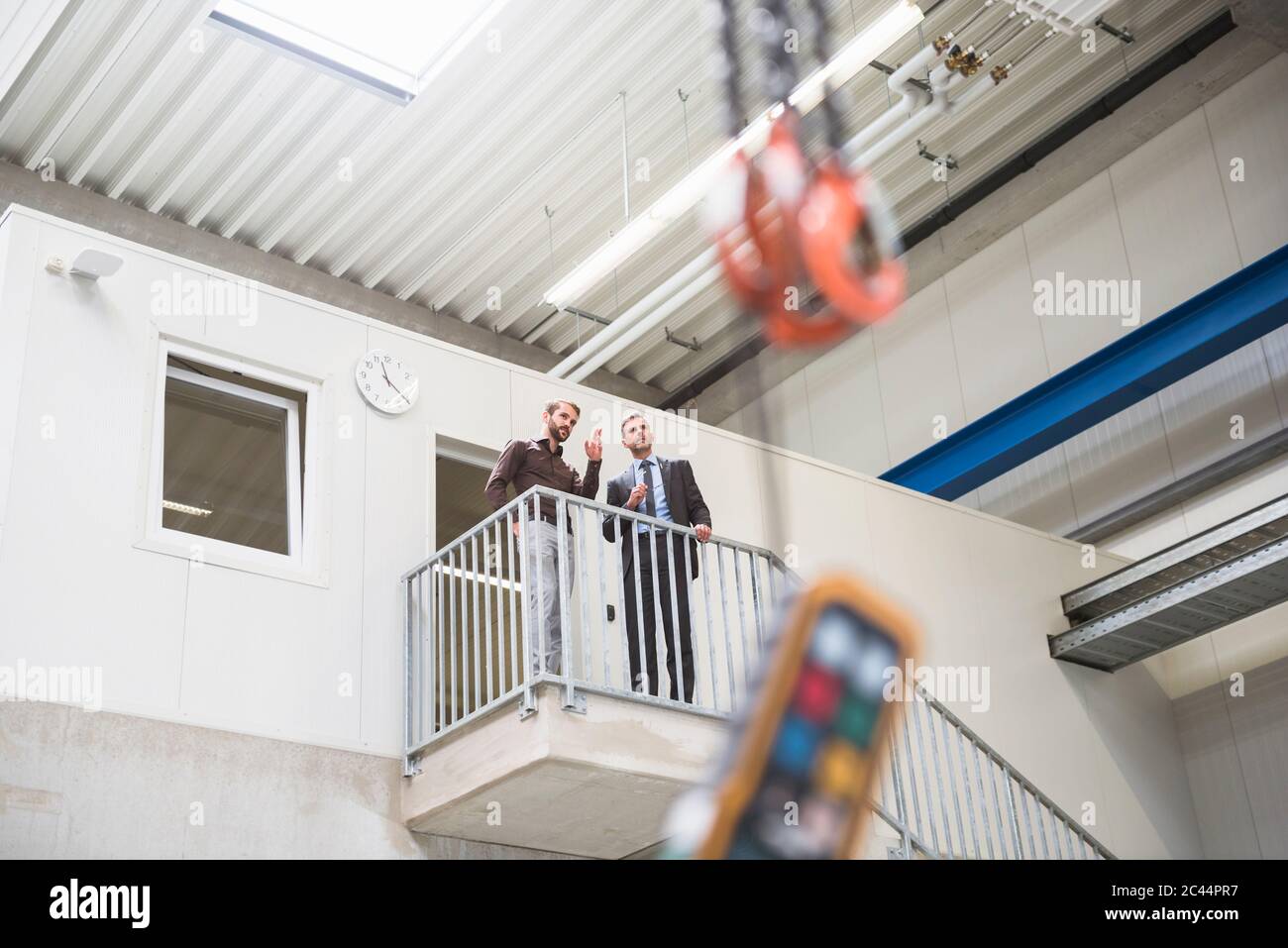 Due uomini d'affari che parlano al piano superiore in una fabbrica Foto Stock
