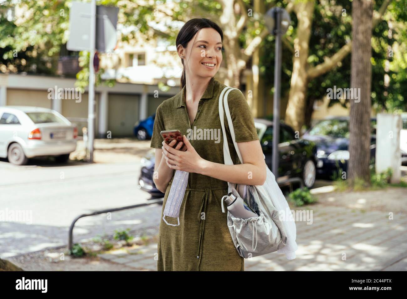 Donna con smartphone che tiene in mano una maschera mentre cammina verso il suo club sportivo Foto Stock
