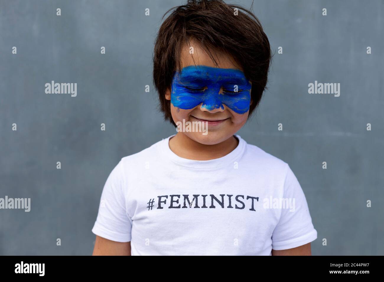 Ritratto di ragazzo sorridente con maschera blu verniciata sul viso con t-shirt con impronta 'Feminista' Foto Stock
