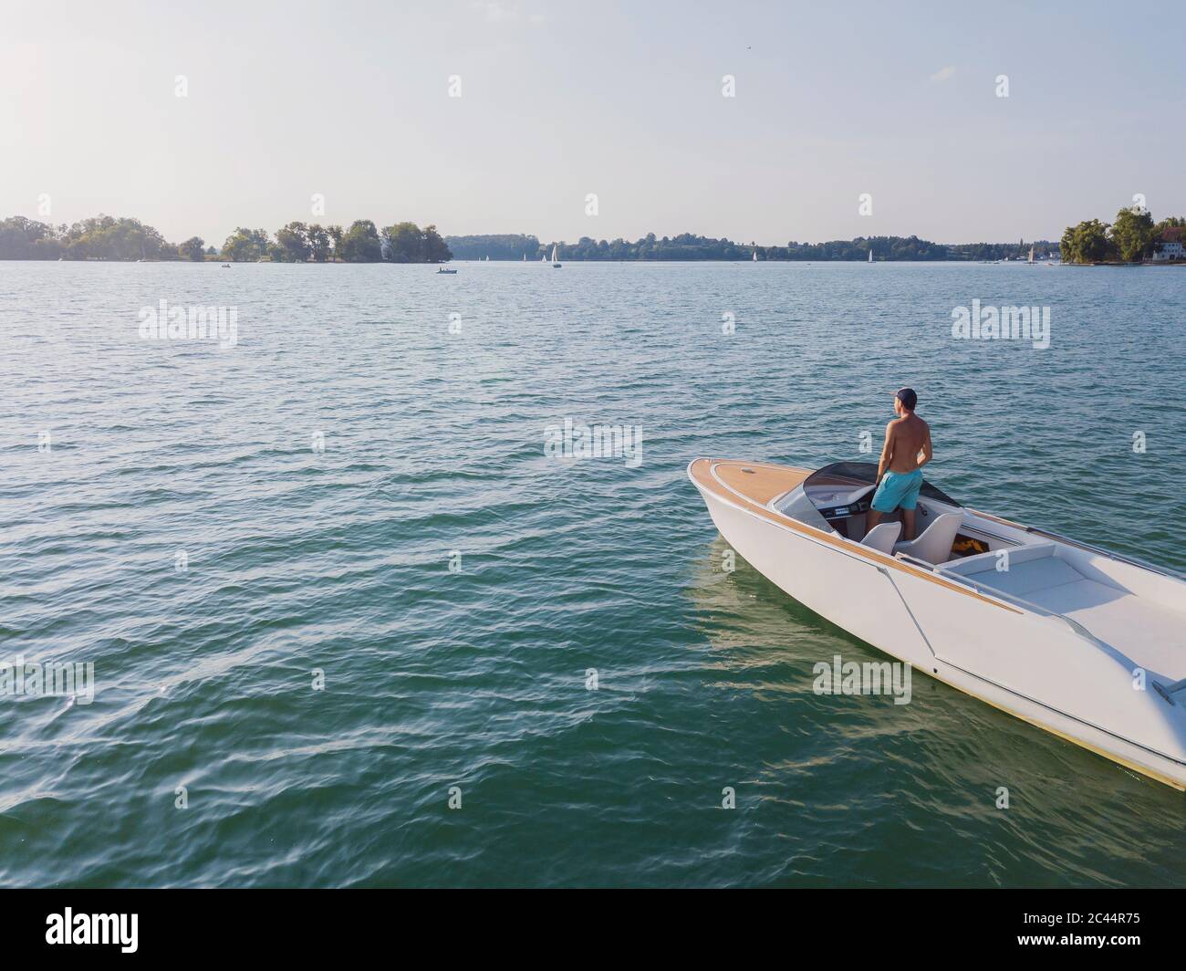 In Germania, in Baviera, Shirtless man standing in motoscafo galleggiante nel lago di Chiemsee ammirando il paesaggio lontano Foto Stock