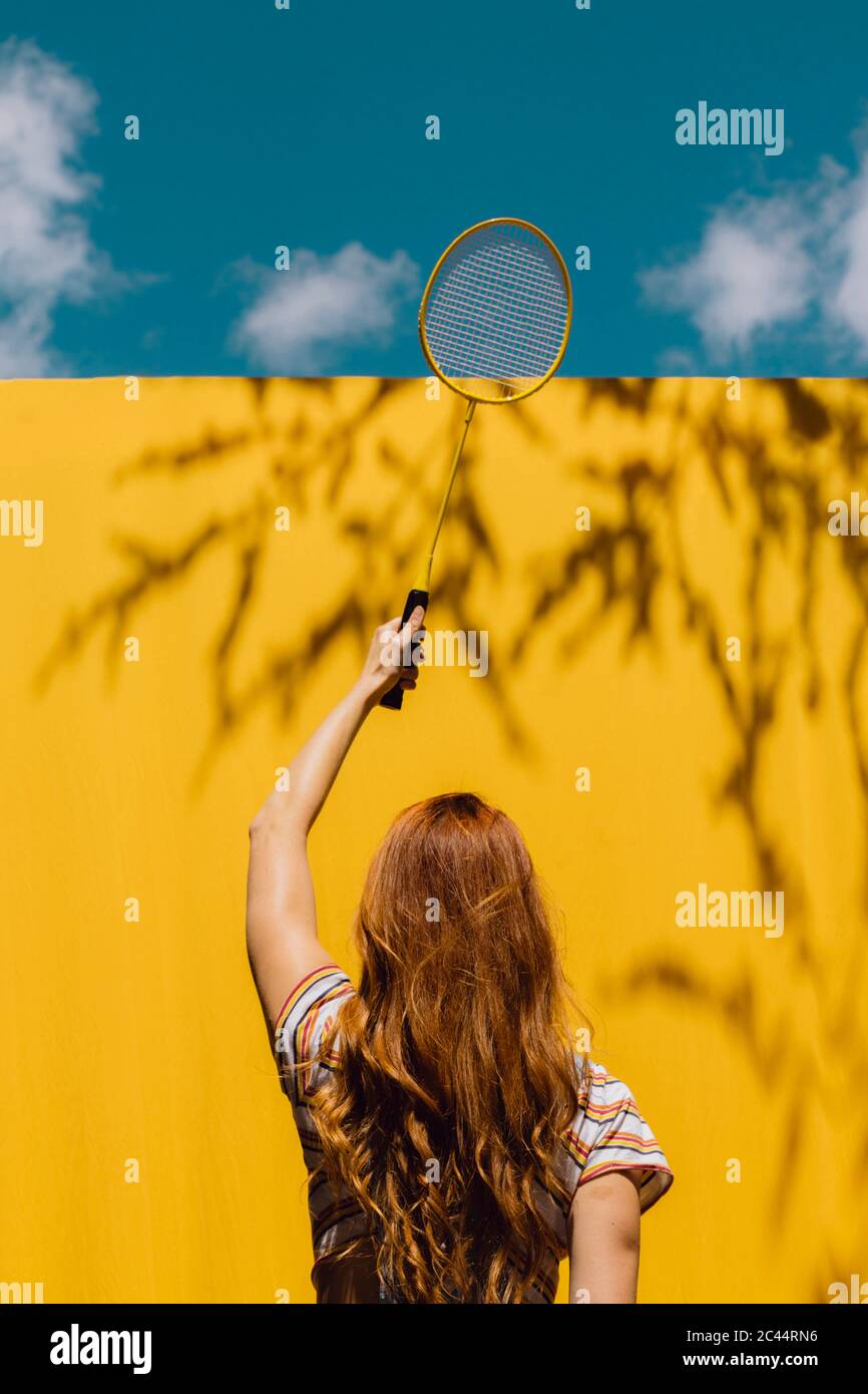 Donna che tiene la racchetta di badminton sopra la parete gialla durante la giornata di sole Foto Stock