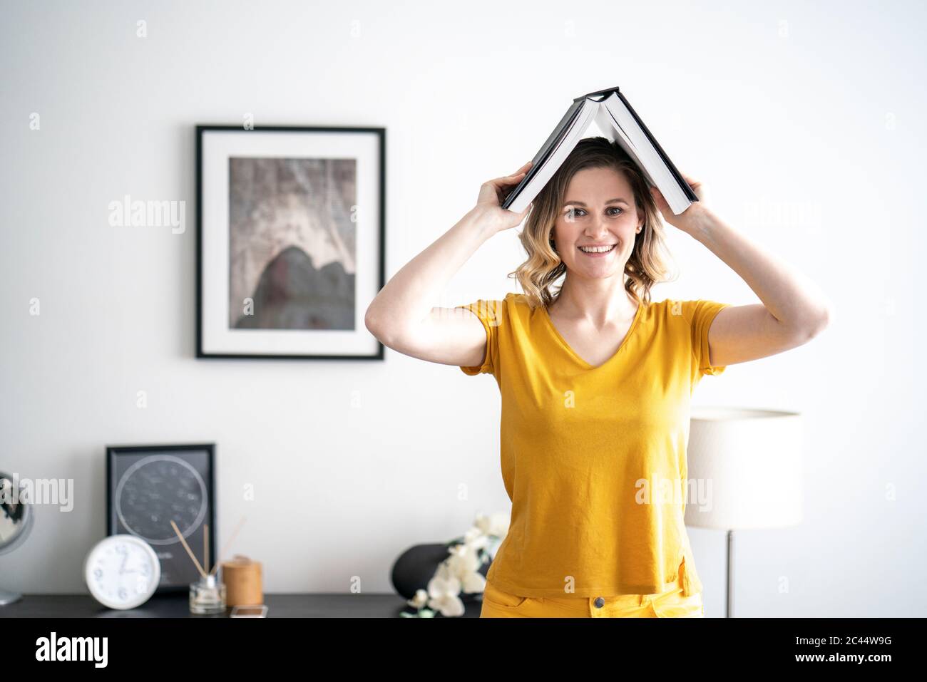Ritratto di donna sorridente a casa tenendo il libro sopra la testa Foto Stock