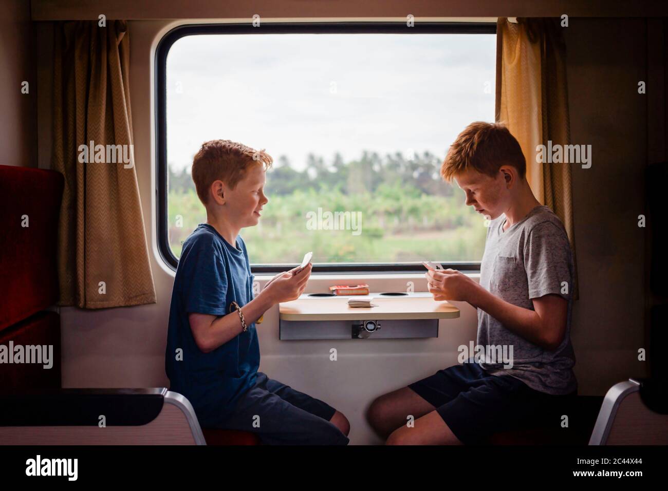 Vista laterale delle carte da gioco dei ragazzi mentre si viaggia in treno, Thailandia, Asia Foto Stock